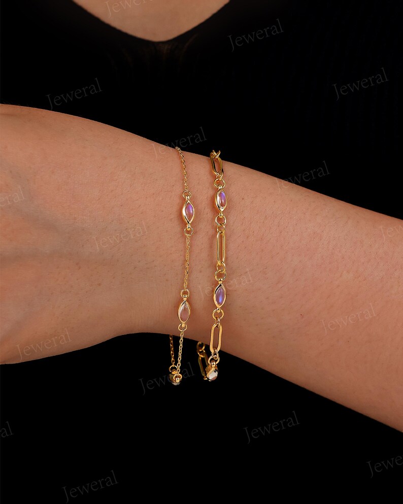 May include: Two gold bracelets are displayed against a dark background. One bracelet features oval-shaped pink gemstones, while the other has a chain link design with similar gemstones. The bracelets are delicate and elegant.