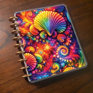 May include: A spiral-bound notebook with a vibrant, colourful design. The cover features a psychedelic pattern of swirling shapes and seashell-like forms in shades of red, orange, yellow, green, blue, and purple. The binding is gold-coloured.