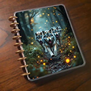 Könnte beinhalten: Ein Spiralplaner mit einem Cover, das eine digitale Illustration von drei Wölfen zeigt, die durch einen Wald laufen. Die Wölfe sind grau und weiß mit gelben Augen. Der Hintergrund ist eine verschwommene Waldszene mit goldenen Kugeln.