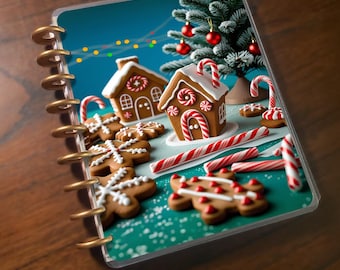 May include: A planner with a Christmas-themed illustration. The image features gingerbread houses, gingerbread men, candy canes, and a small Christmas tree with red ornaments. The planner has a gold spiral binding and is set against a teal background.
