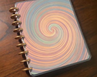 May include: A spiral-patterned notebook cover with a clear plastic overlay. The design features a swirling pattern of pastel colors, including peach, blue, and green. The notebook has gold-colored binding rings.