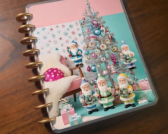 May include: A planner with a Christmas-themed design. The cover features a silver Christmas tree with colorful ornaments, Santa Claus figurines, and a pink and teal background. The planner has a gold spiral binding.