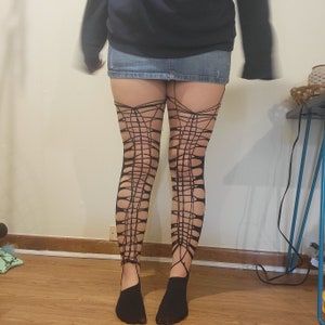 May include: Black fishnet stockings with a spiderweb design. The stockings are worn on a person's legs.