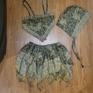 May include: A three-piece set featuring a green paisley pattern. The set includes a halter top, a skirt, and a head covering. The skirt and top have fringe detailing. The fabric has a gold and white design.