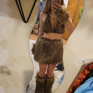 May include: A woman wearing a brown furry costume with a matching headband, skirt, leg warmers, and gloves. The costume is made of faux fur and has a wild animal theme.
