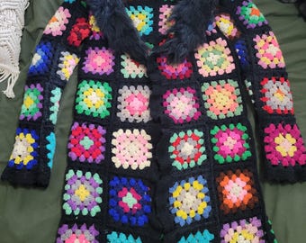 May include: A long, black crochet coat featuring colorful granny squares and a black faux fur collar. The coat has long sleeves and a unique, handmade aesthetic, perfect for a vintage or bohemian style.