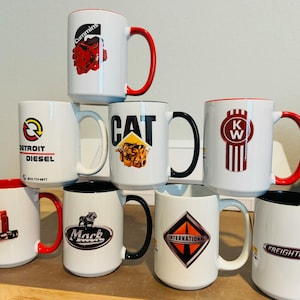 May include: Eight white ceramic mugs with black and red rims. Each mug features a different logo of a popular truck brand, including Cummins, Detroit Diesel, CAT, Kenworth, Mack, International, and Freightliner.