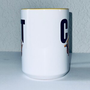 May include: White ceramic mug with a yellow rim. The mug has a black and yellow graphic of a construction vehicle with the word "CAT" printed on the side.