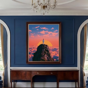 Puede incluir: Una impresión artística enmarcada representa a una persona de pie en la cima de una montaña, frente a un sol poniente. La obra de arte presenta un cielo vibrante con tonos naranja, rosa y azul, y un mar de nubes. La impresión se exhibe en una habitación con paredes azules y un mueble de madera.