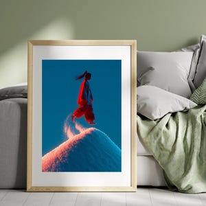 Puede incluir: Una impresión artística enmarcada que presenta a una persona con ropa roja saltando desde una cima cubierta de nieve contra un fondo azul vibrante. La obra de arte está iluminada con luces rojas y azules, creando una escena dramática y dinámica.