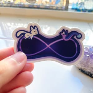 Könnte beinhalten: Ein Aufkleber mit zwei Comic-Tieren, einem weißen und einem violetten, die auf einem Unendlichkeitszeichen sitzen. Das Zeichen ist weiß umrandet und mit einem dunkelvioletten Farbverlauf gefüllt.