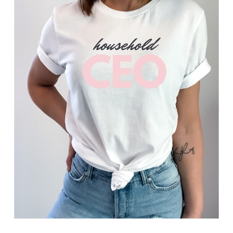 May include: White t-shirt with the words "household CEO" printed on the front. The word "household" is in a dark blue script, and "CEO" is in a light pink, bold font. The shirt is tied at the waist.
