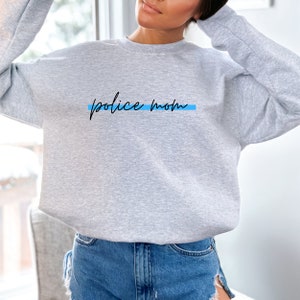 May include: Gray sweatshirt with the text "police mom" in black script with a thin blue line underneath.