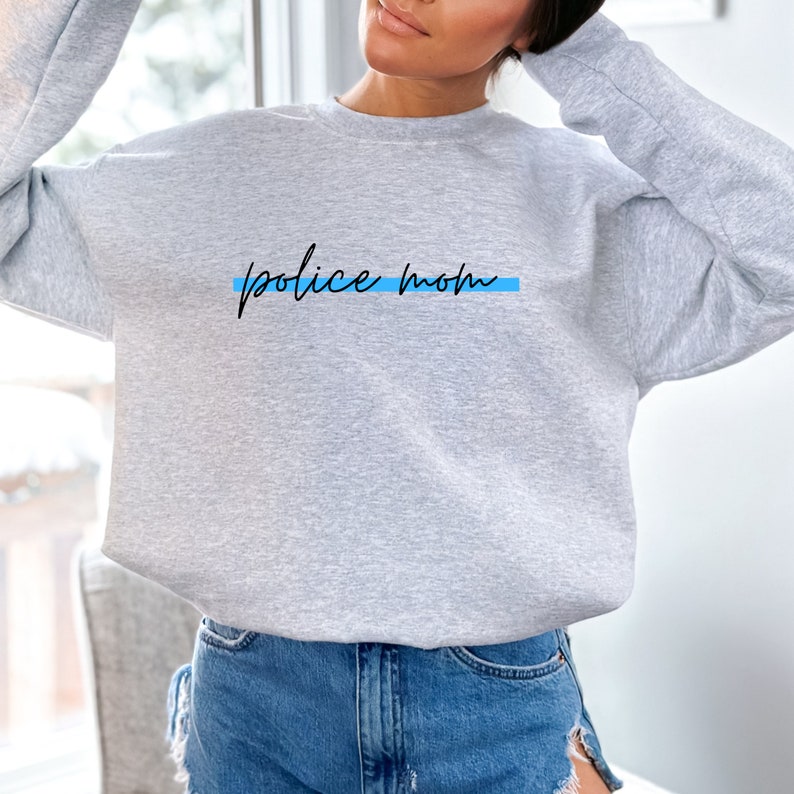 May include: Gray sweatshirt with the text "police mom" in black script with a thin blue line underneath.