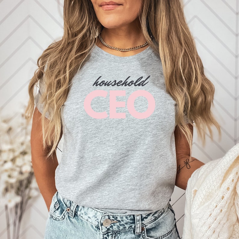 May include: A light gray t-shirt with the words "household CEO" printed on the front in black script and pink block letters. The shirt is a crew neck style and is made of a soft material.