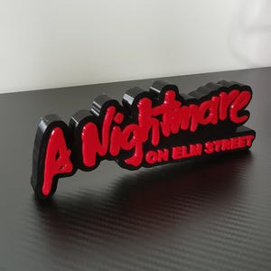 Può includere: Un logo di "A Nightmare on Elm Street", stampato in 3D in nero con lettere rosse.
