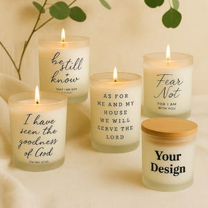 Puede incluir: Cinco velas blancas encendidas con citas inspiradoras en escritura negra. Una vela tiene una tapa de madera. Hojas verdes de eucalipto en el fondo. Las velas están sobre una superficie de color crema.