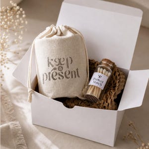 May include: A white cardboard gift box containing a beige drawstring pouch with the text "keep & present" printed in dark ink, and a small glass bottle with a cork stopper filled with matches, featuring a label that reads "Perfect Match".