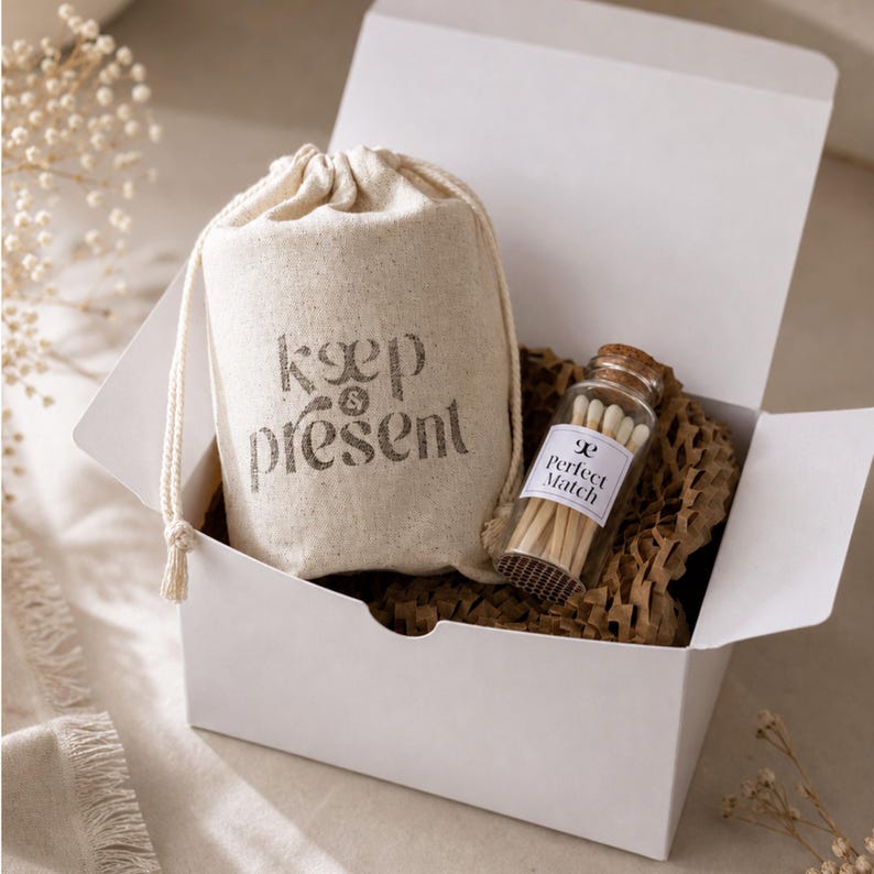May include: A white cardboard gift box containing a beige drawstring pouch with the text "keep & present" printed in dark ink, and a small glass bottle with a cork stopper filled with matches, featuring a label that reads "Perfect Match".