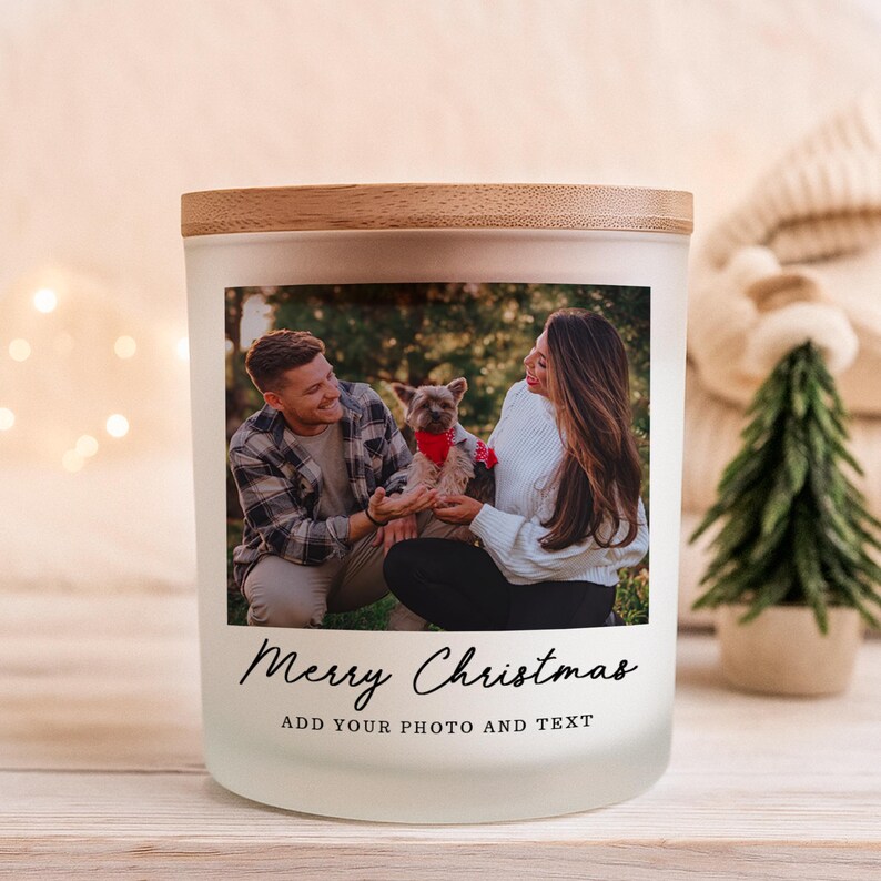 May include: A frosted glass candle jar with a wooden lid featuring a custom photograph of a person, a dog, and another person. Below the photo, the text reads Merry Christmas and ADD YOUR PHOTO AND TEXT in a black, elegant script and sans-serif font.