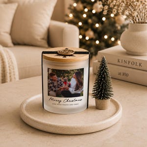 May include: A frosted glass candle jar with a wooden lid and a black band featuring a gold wax seal. The front displays a custom photograph of a couple with a dog, with the printed text Merry Christmas and ADD YOUR PHOTO AND TEXT below it.