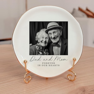 May include: A white decorative plate with a gold rim and a gold stand. The plate features a black and white photo of an elderly couple. The text "Dad and Mom FOREVER IN OUR HEARTS" is below the photo.