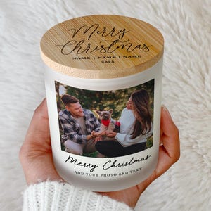 May include: A frosted glass candle jar with a bamboo lid featuring the text Merry Christmas, NAME | NAME | NAME, and 2025. The jar displays a color photograph of two people and a dog, with the text Merry Christmas ADD YOUR PHOTO AND TEXT below.