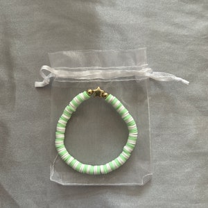 May include: A green and white beaded bracelet with a gold star charm. The bracelet is in a white organza bag.