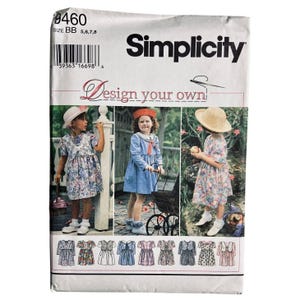 May include: Simplicity sewing pattern packet featuring a variety of children's dress designs. The packet has the text "Design your own" and includes images of children wearing the dresses. The packet is white with black text and a barcode.