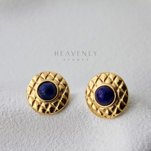 Op de afbeelding: Een paar gouden oorbel studs met een blauwe lapis lazuli steen in elk. De oorbellen hebben een textuur, geometrisch ontwerp.