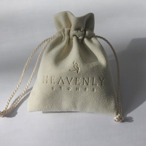 May include: A white velvet drawstring bag with the text "HEAVENLY STONES" printed on the front.