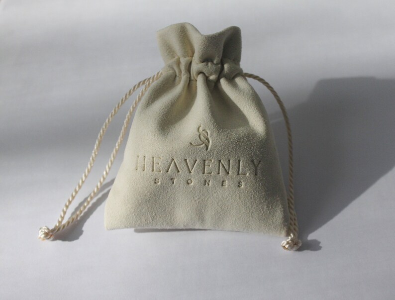 May include: A white velvet drawstring bag with the text "HEAVENLY STONES" printed on the front.