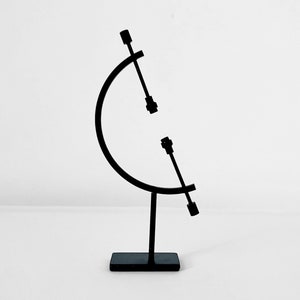 May include: A black metal sculpture with a circular base and two arms extending upwards. The arms are connected to the base by a curved metal piece.