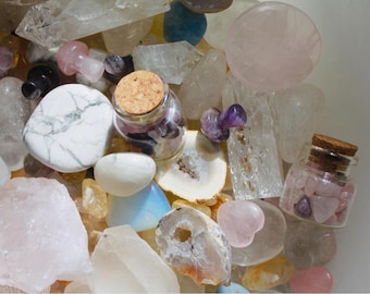 May include: A collection of various crystals and stones in a bowl, including clear quartz, rose quartz, amethyst, and white agate. Two small glass jars with cork tops contain smaller crystals.