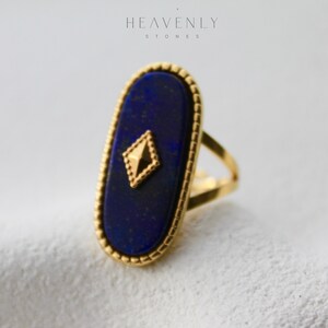 May include: A gold ring with a large oval lapis lazuli stone set in a gold bezel. The stone has a gold diamond-shaped accent in the center.