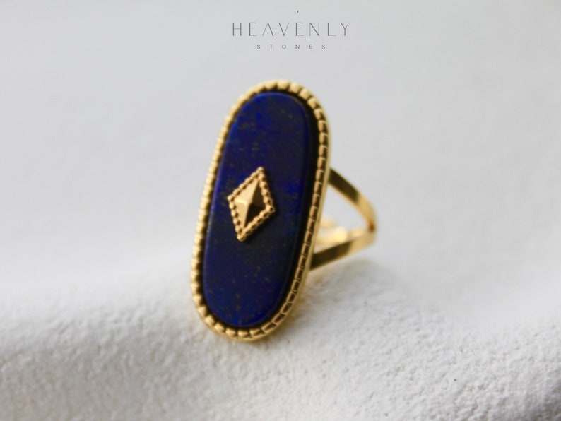 May include: A gold ring with a large oval lapis lazuli stone set in a gold bezel. The stone has a gold diamond-shaped accent in the center.