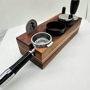 May include: A wooden espresso stand with a black and silver portafilter, a black tamper, and a black and silver tamper base. The stand has a light wood grain and a dark wood grain.