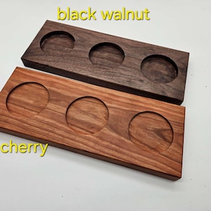 May include: Two wooden drink coasters, one black walnut and one cherry, each with three circular indentations. The black walnut coaster is a dark brown, while the cherry coaster is a reddish-brown.