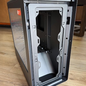 以下が含まれることがあります： 黒いコンピューターケースで、透明なサイドパネルが付いています。内部フレームはシルバーです。ケースは開いており、内部構造が見えます。「Fragile」と書かれた小さなステッカーがガラスに貼られています。