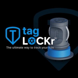May include: A digital illustration of a cylindrical device with a blue base and a gray body. The device has a shield-shaped logo with a blue "T" inside, and the text "tag LOCKr" in blue and white. The tagline reads "The ultimate way to track your ride."