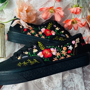 Könnte beinhalten: Schwarze Canvas-Sneaker mit niedrigem Schaft und bunter Blumenstickerei. Die Stickerei zeigt rosa, rote und grüne Blumen.