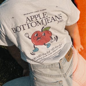 White unisex cotton t-shirt with a quirky fruit design and Flo Rida’s iconic “Low” lyrics on the back