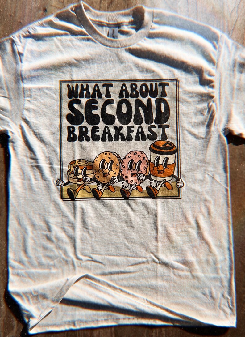 Unisex beige shirt with a retro graphic of breakfast foods and “What About Second Breakfast” text, perfect for LOTR fans.