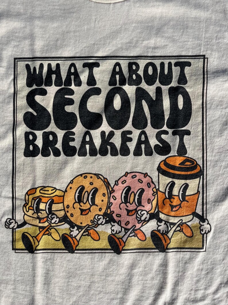 detail of the retro graphic of breakfast and title “what about second breakfast” perfect shirt for lord of the rings fans