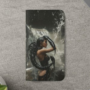 Pode incluir: Uma capa de telefone preta com uma impressão de arte fantástica de uma mulher em uma cachoeira. A mulher está vestindo roupas pretas e tem um design escuro, semelhante a tentáculos, ao seu redor. O fundo mostra uma cachoeira.