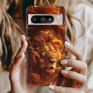 May include: A phone case featuring a majestic lion with a fiery mane and a background of flames. The design is predominantly warm tones of orange, red, and gold, creating a dramatic and powerful aesthetic. The case has a sleek, modern design.