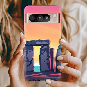 Puede incluir: Una funda de teléfono rosa con una escena de puesta de sol y una silueta de Stonehenge. La funda del teléfono tiene una carcasa de cámara negra con tres lentes.