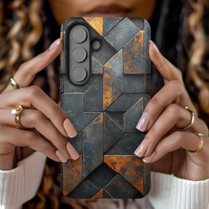 May include: A smartphone case with a geometric design. The case features a pattern of dark gray and rust-colored rectangular shapes. The phone case has a black camera module with three lenses.