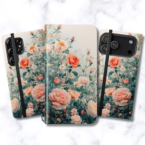 May include: A rectangular phone case featuring a floral pattern of peach and pink roses with green foliage on a cream background. The case includes a black elastic strap across the front and a cutout for the camera lens on the back.