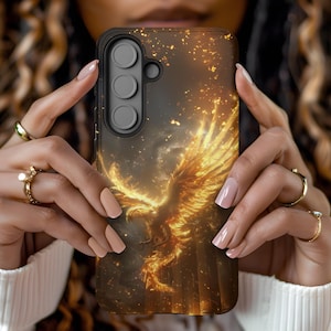 May include: A phone case featuring a fiery phoenix design. The case has a black border and a detailed illustration of a golden phoenix with outstretched wings against a dark, smoky background. The design includes sparks and a sense of movement.
